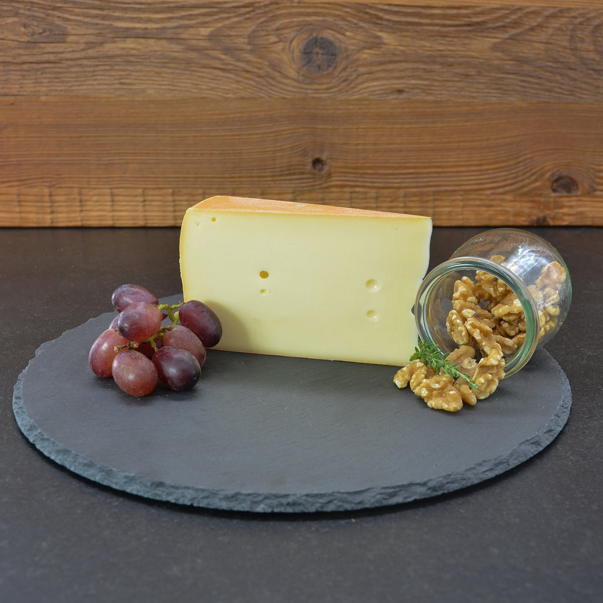 Stück Almkäse von vorne, umgeben von Walnüssen und Weintrauben